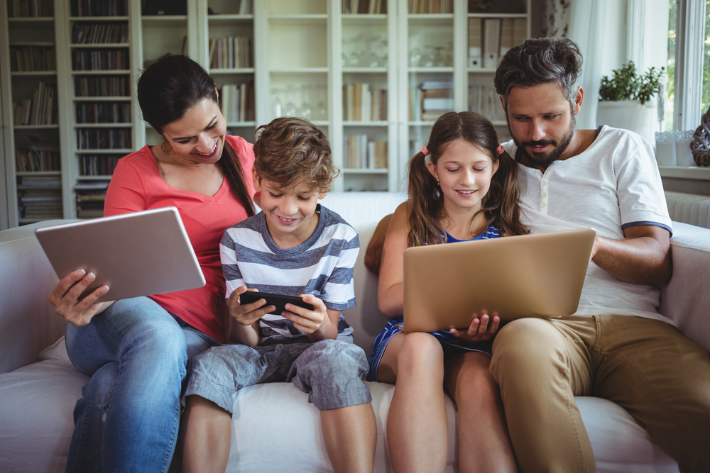 Happy family sitting on sofa and using laptop, mobile phone and digital tablet at home-1